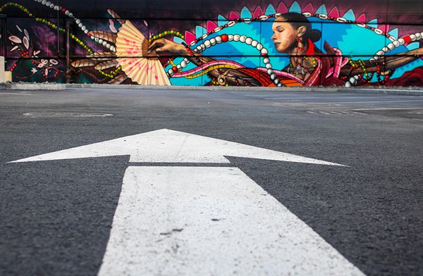 Arrow on the ground pointint to a modern mural of a indigenous Mexican woman, Undergound Inkblock mural by Victor Quiñonez